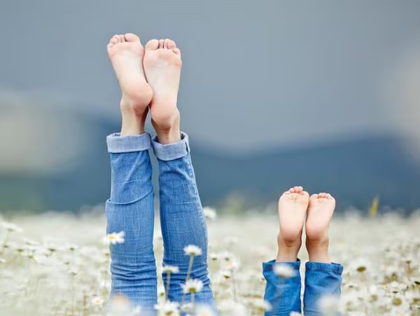 Zwei Personen strecken barfuss die Beine in einem Blumenfeld – Symbolbild fuer gesunde Fuesse im Sommer.