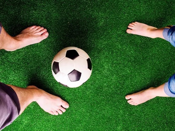 Kinder- und Maennerfuesse auf Kunstrasen mit Fussball – gemeinsame Aktivitaet und Fussgesundheit.